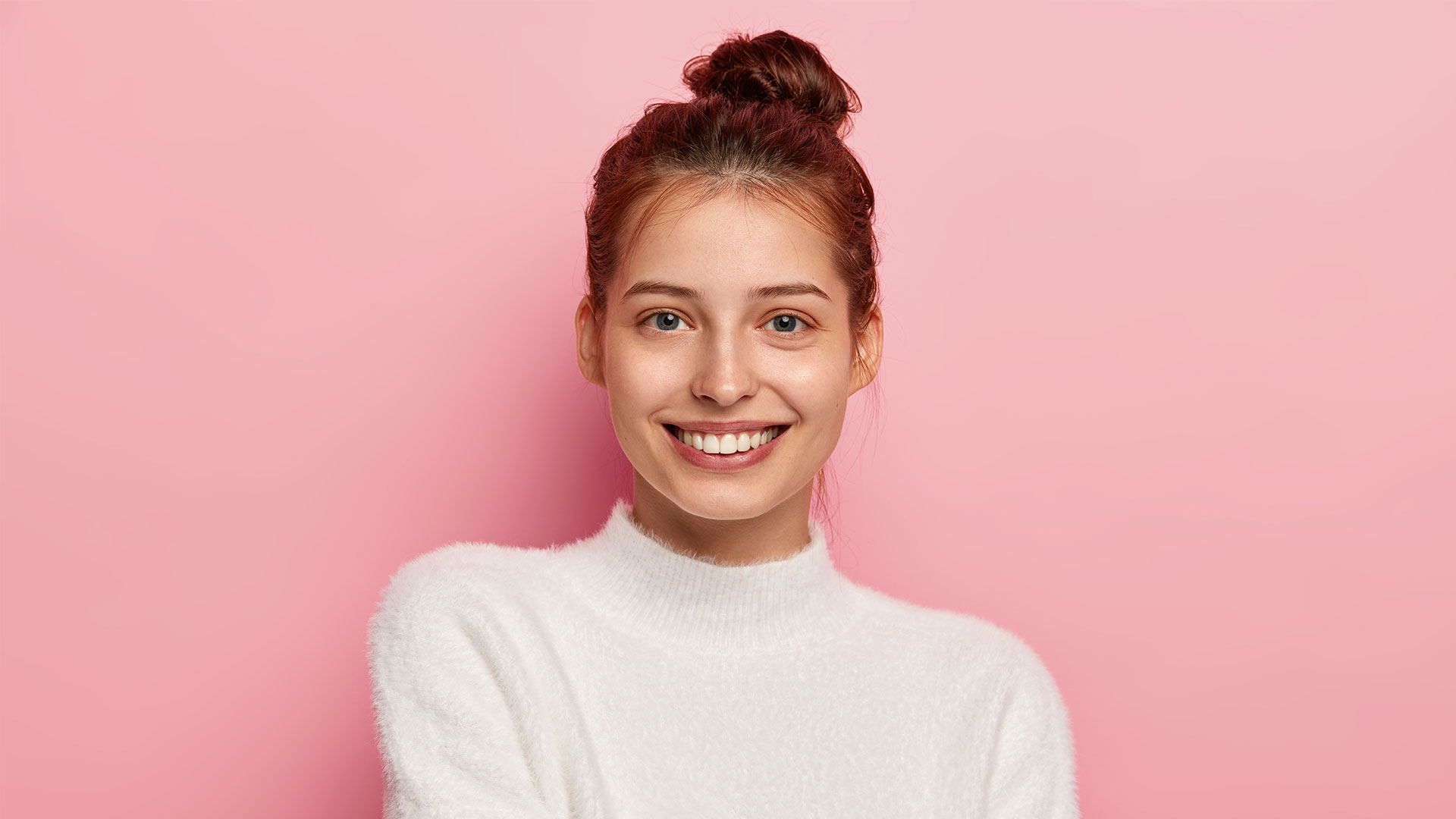 Une jeune femme sourit devant un fond rose.