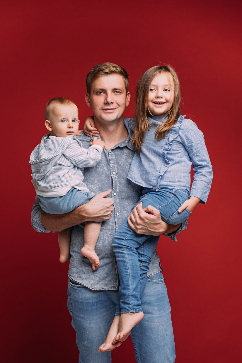Un homme souriant tient deux enfants dans ses bras.