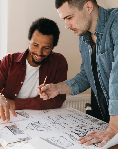 Un homme montre sur un plan d'architecte quelque chose à un autre.