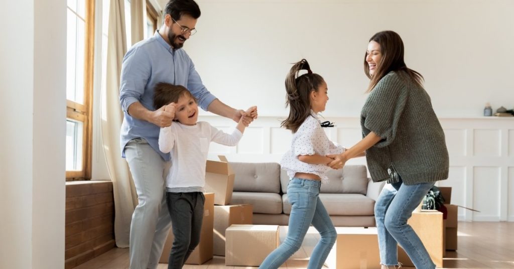 Un couple et leurs deux enfants, joyeux, sautant dans le salon parmi des cartons prêts à être remplis