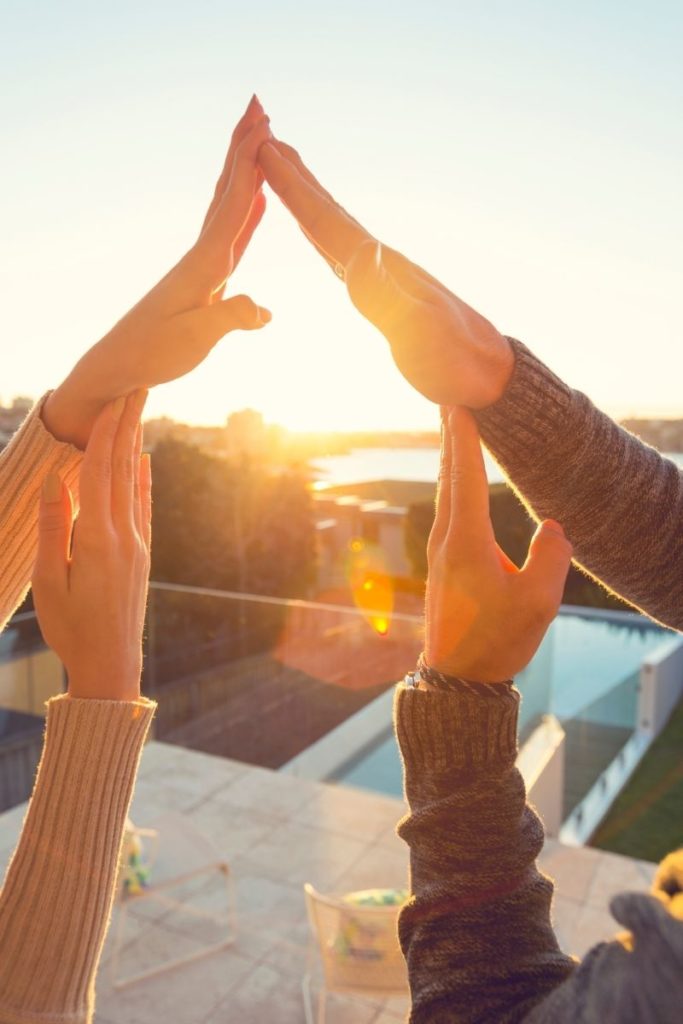 Un couple formant une silhouette de maison avec leurs bras, face à un jardin dégagé