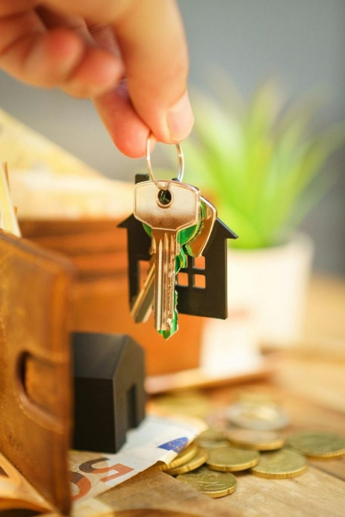 Une main tenant un trousseau de clés au-dessus d’un porte-monnaie ouvert, avec des billets et des pièces posés sur une table