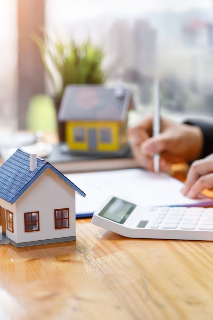 Un homme rédige sur une feuille, avec devant lui une maquette de maison et une calculatrice