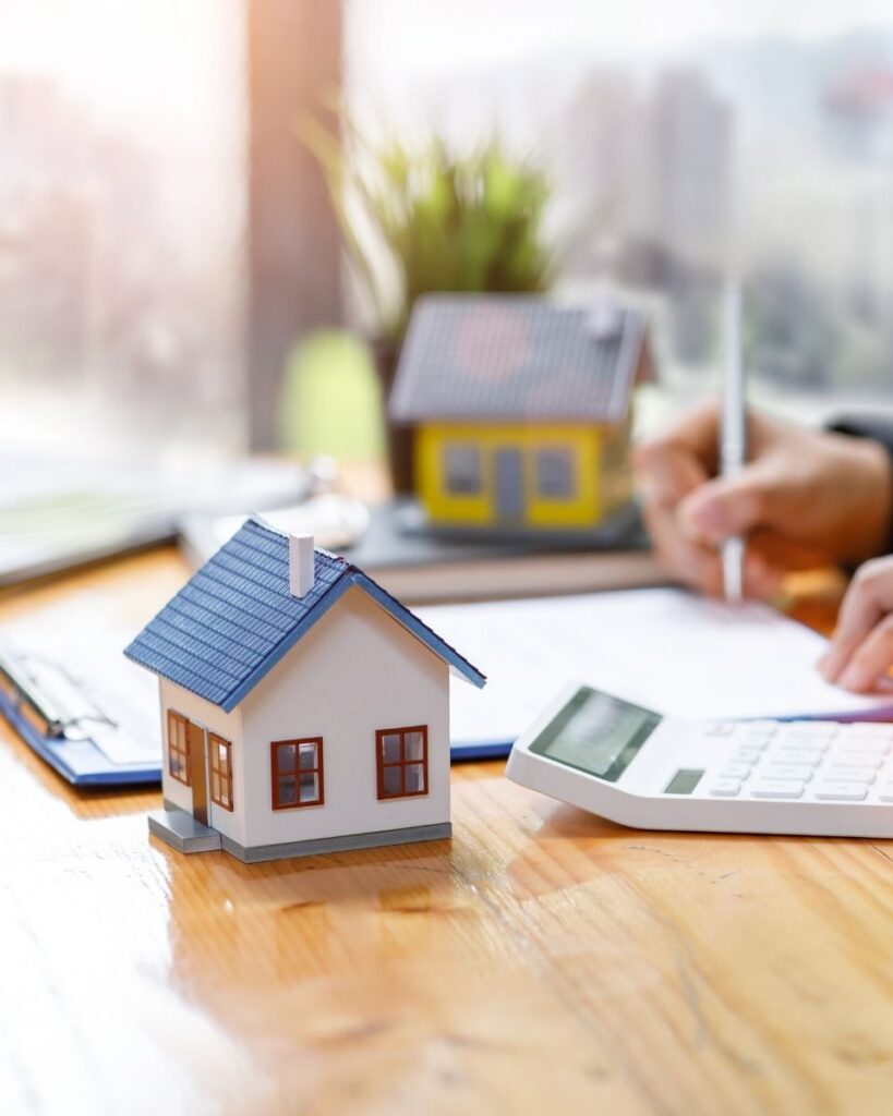 Un homme rédige sur une feuille, avec devant lui une maquette de maison et une calculatrice