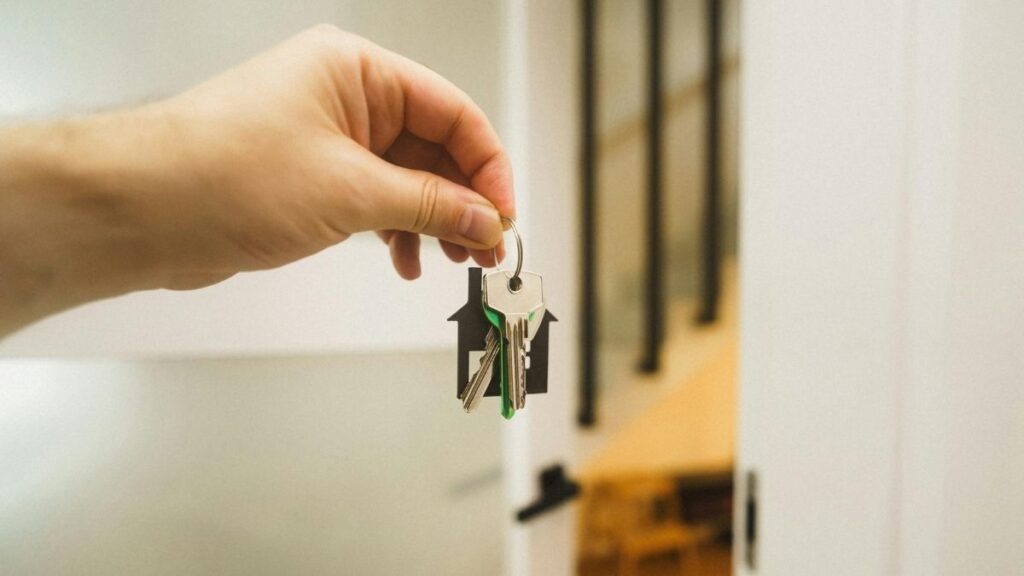 Homme tendant un trousseau de clés devant l’entrée intérieure d’une maison