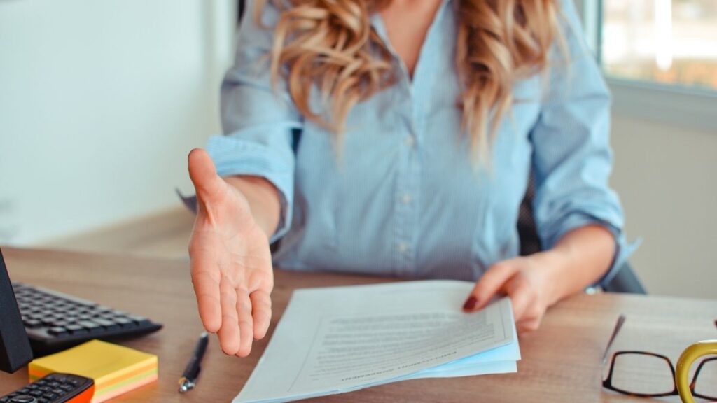 Femme installée à son bureau, tenant un dossier dans sa main, prête à effectuer une poignée de main