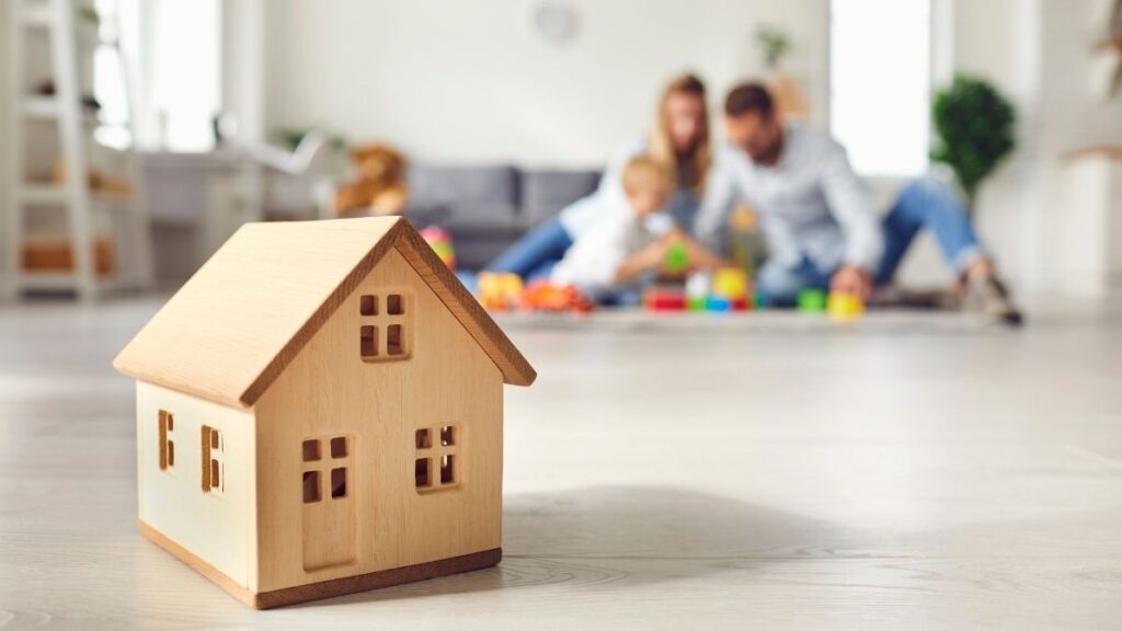 Une maison en bois avec, en arrière-plan, un couple et leur enfant en train de jouer