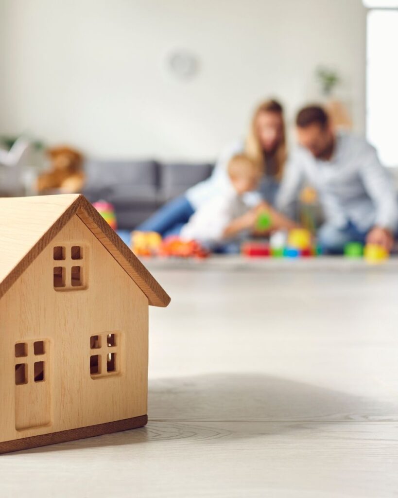 Une maison en bois avec, en arrière-plan, un couple et leur enfant en train de jouer