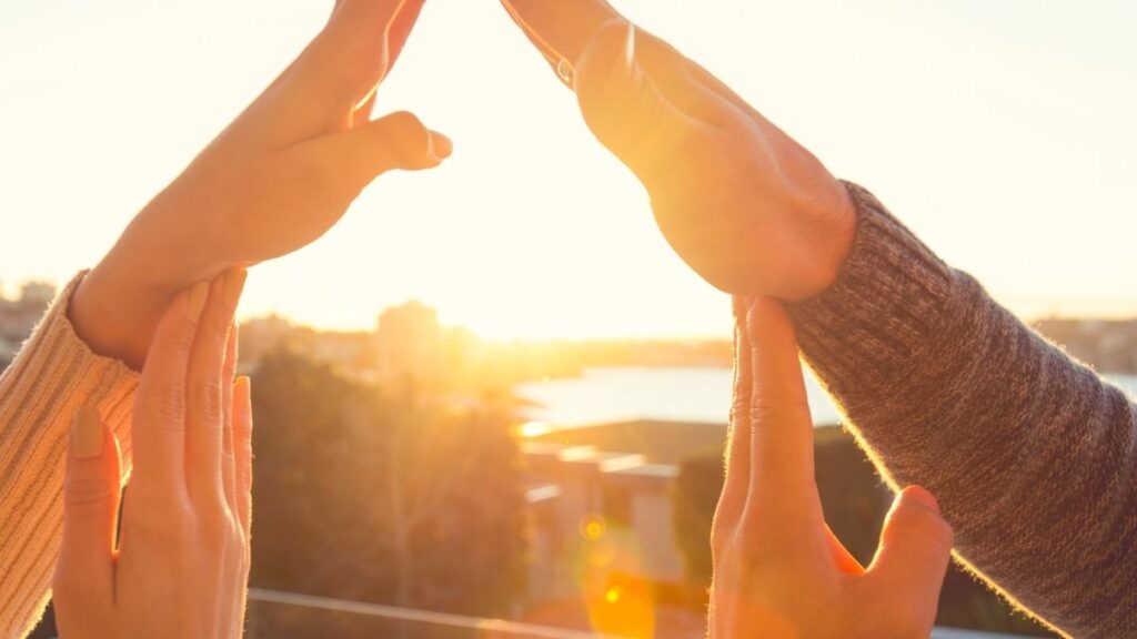 Un couple formant une silhouette de maison avec leurs bras, face à un jardin dégagé