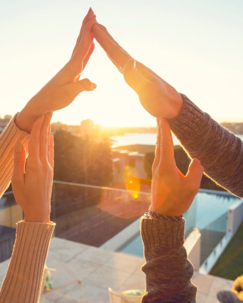 Un couple formant une silhouette de maison avec leurs bras, face à un jardin dégagé