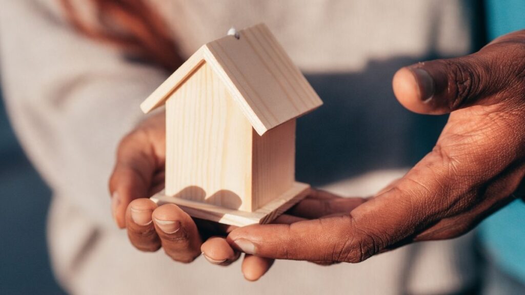Un couple tient une petite maison en bois dans ses mains, dont seules les mains sont visibles