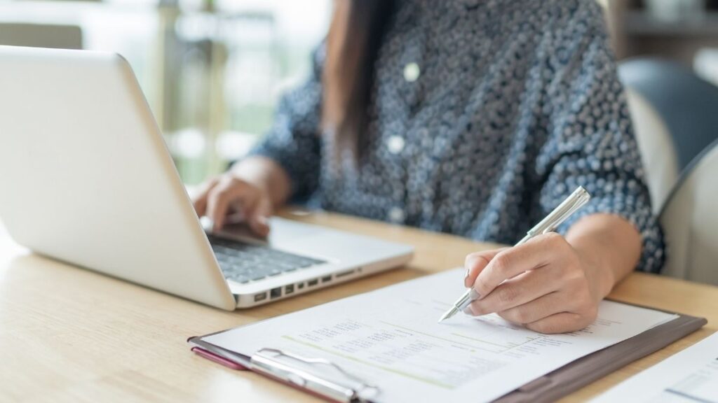 Femme devant un ordinateur portable en train de prendre des notes