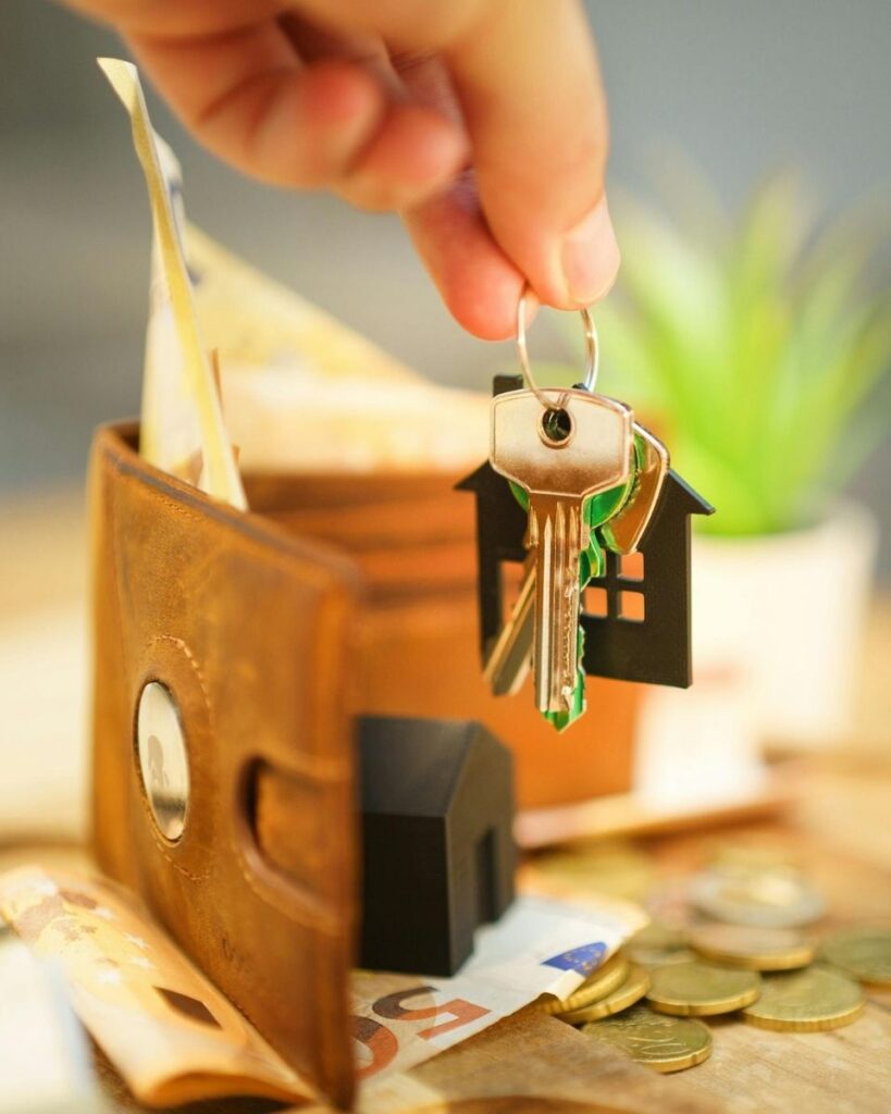 Une main tenant un trousseau de clés au-dessus d’un porte-monnaie ouvert, avec des billets et des pièces posés sur une table